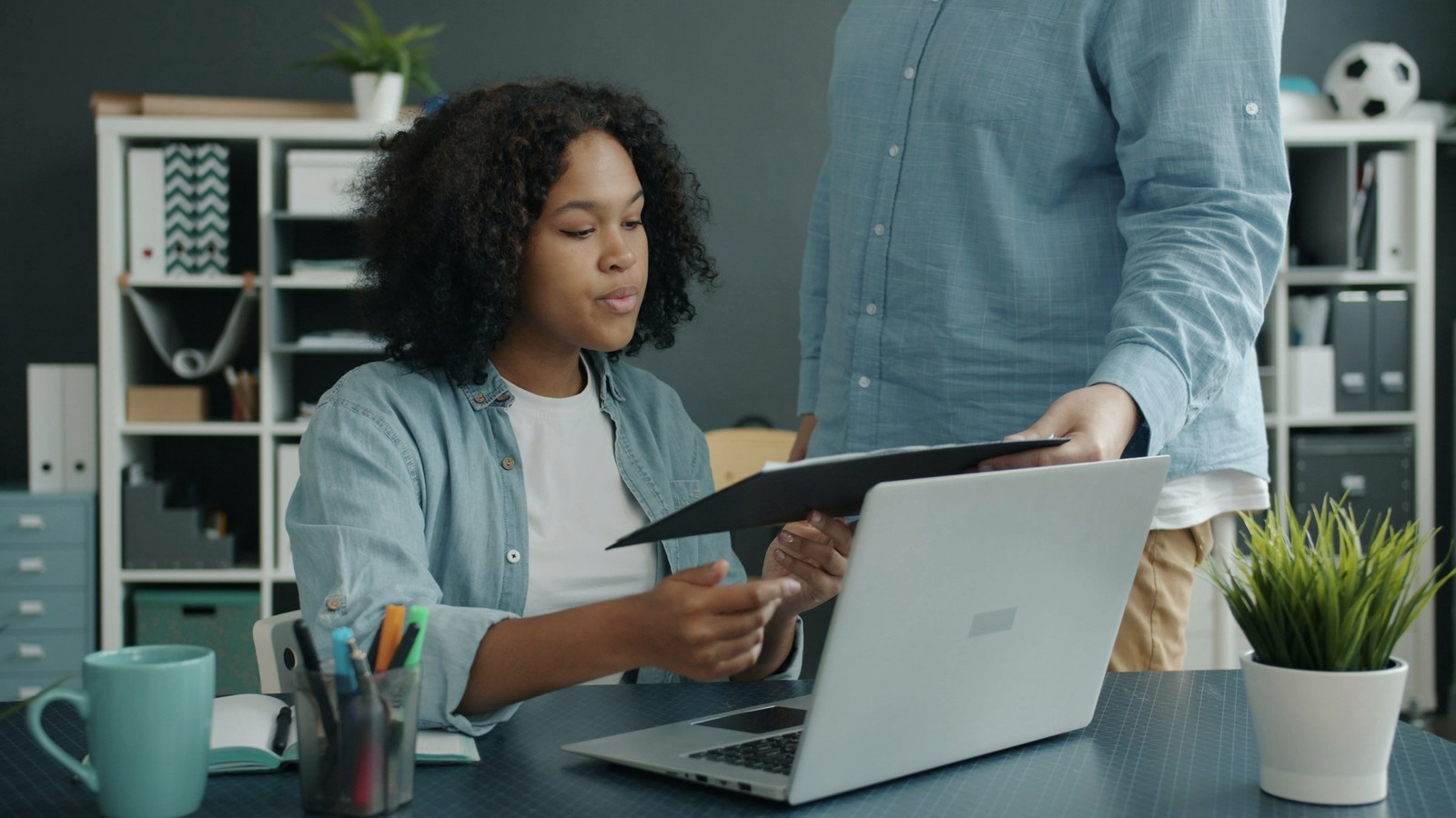 Two colleagues review a paper record beside an open laptop in a quiet office.